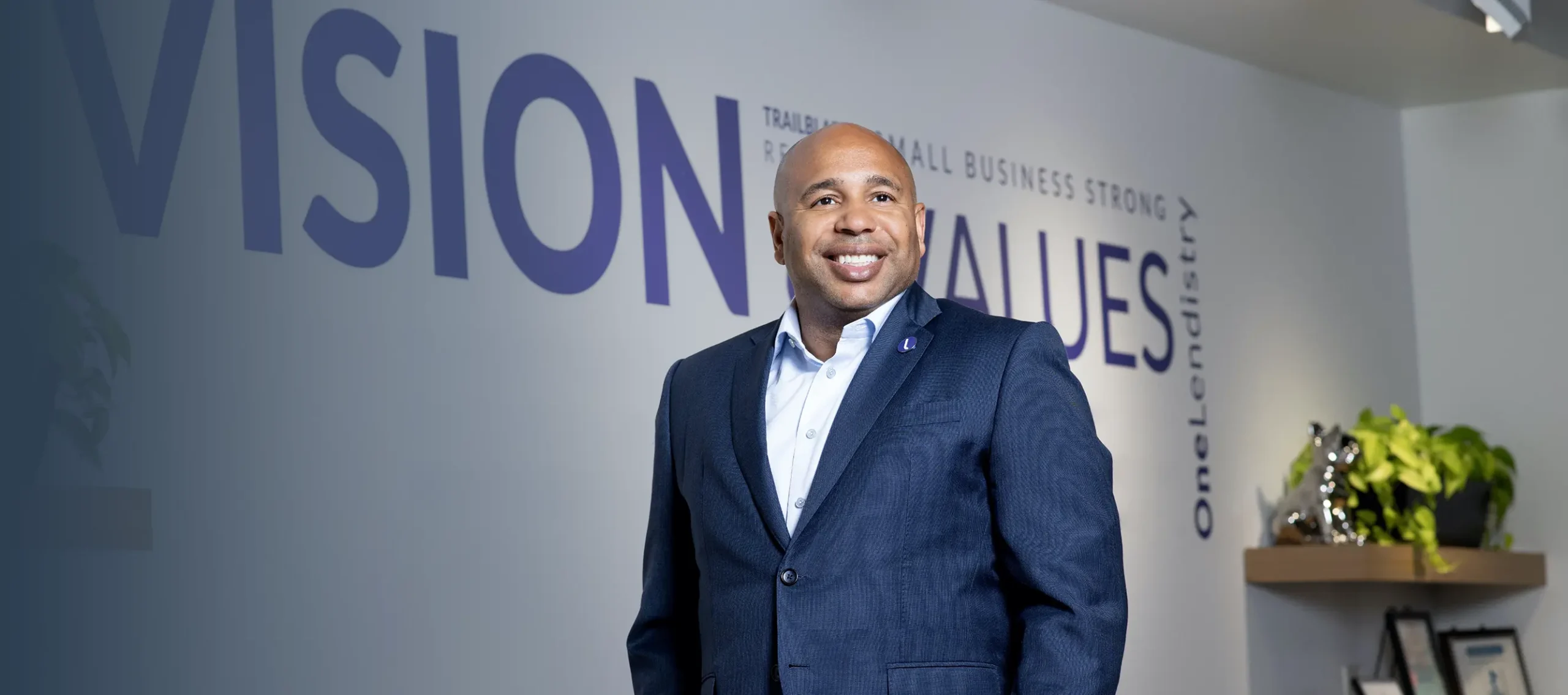 Everett standing at the office building in front of a wall with Vision & Values in purple text with motivational text in smaller font surround it
